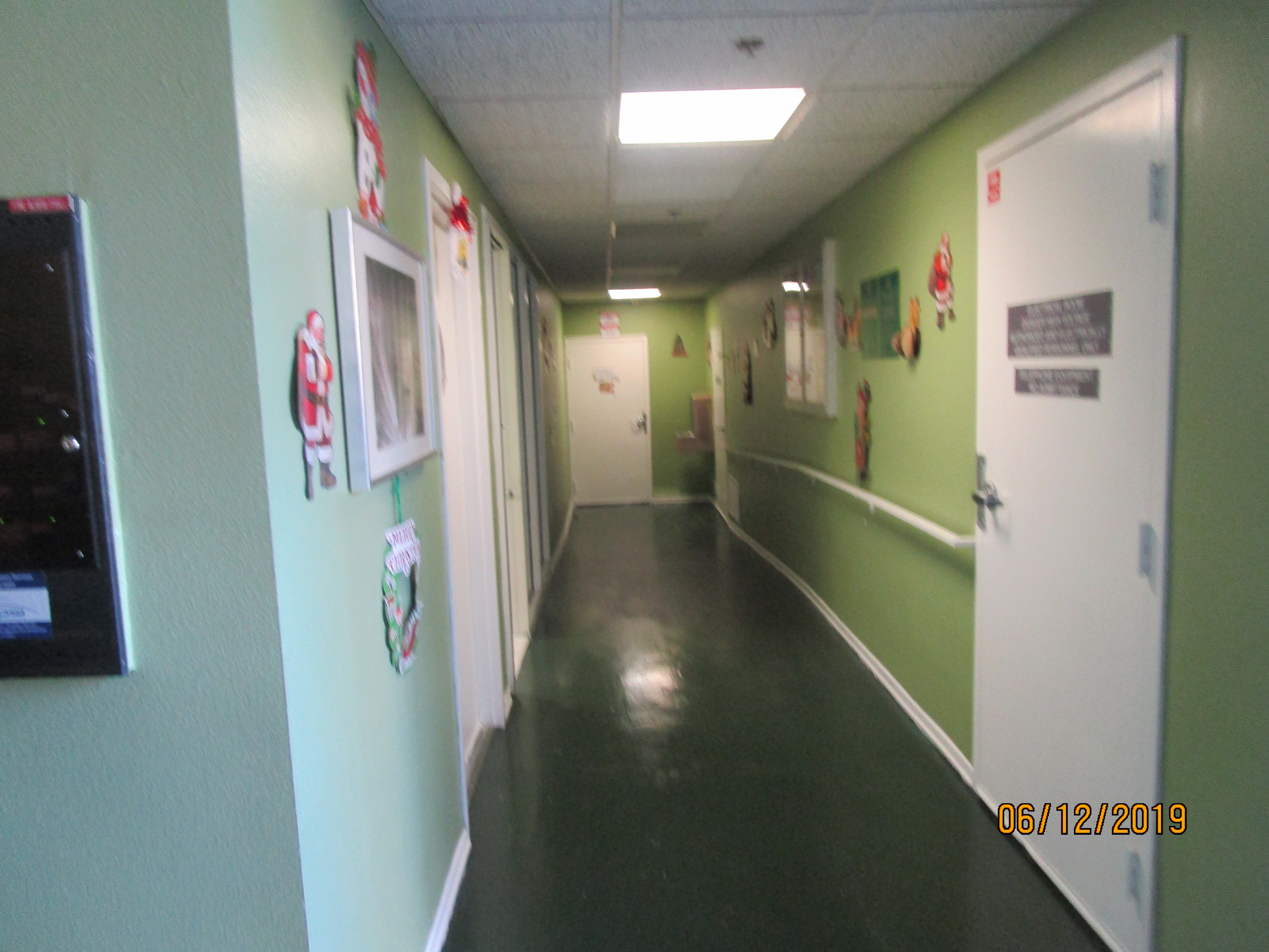 View of a hall, green linoleum floors, light green walls, handrails on the right side wall, Christmas decorations all over.