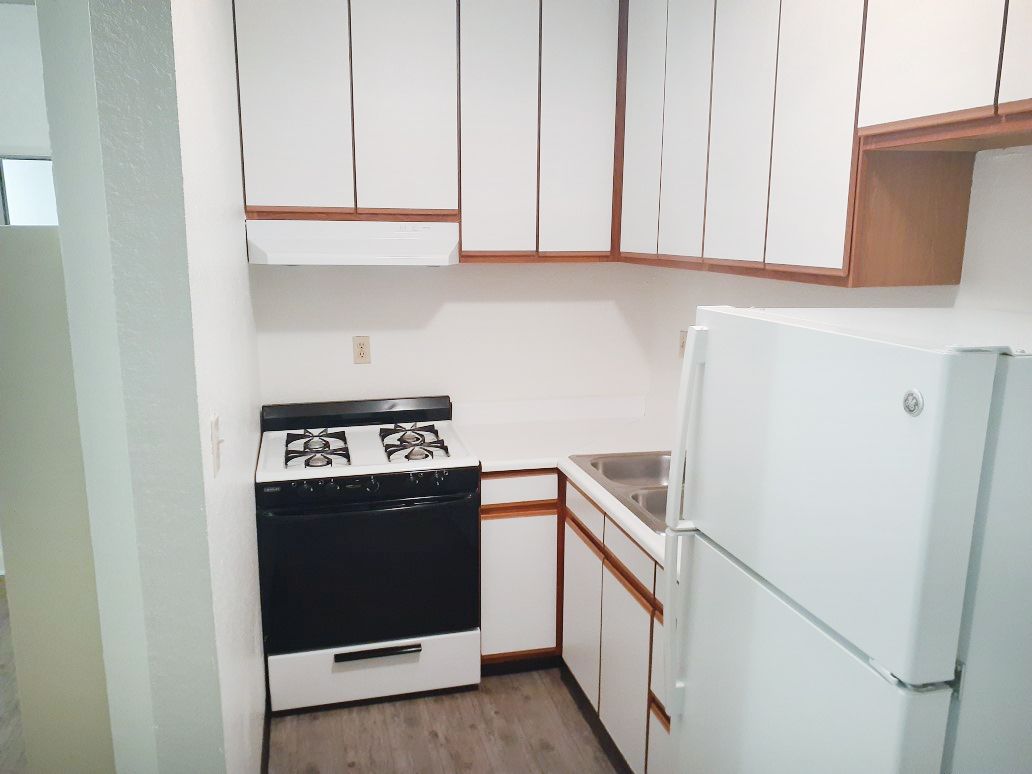 Interior view of a kitchen in a unit showing a stove, refrigerator, sink and cabinets