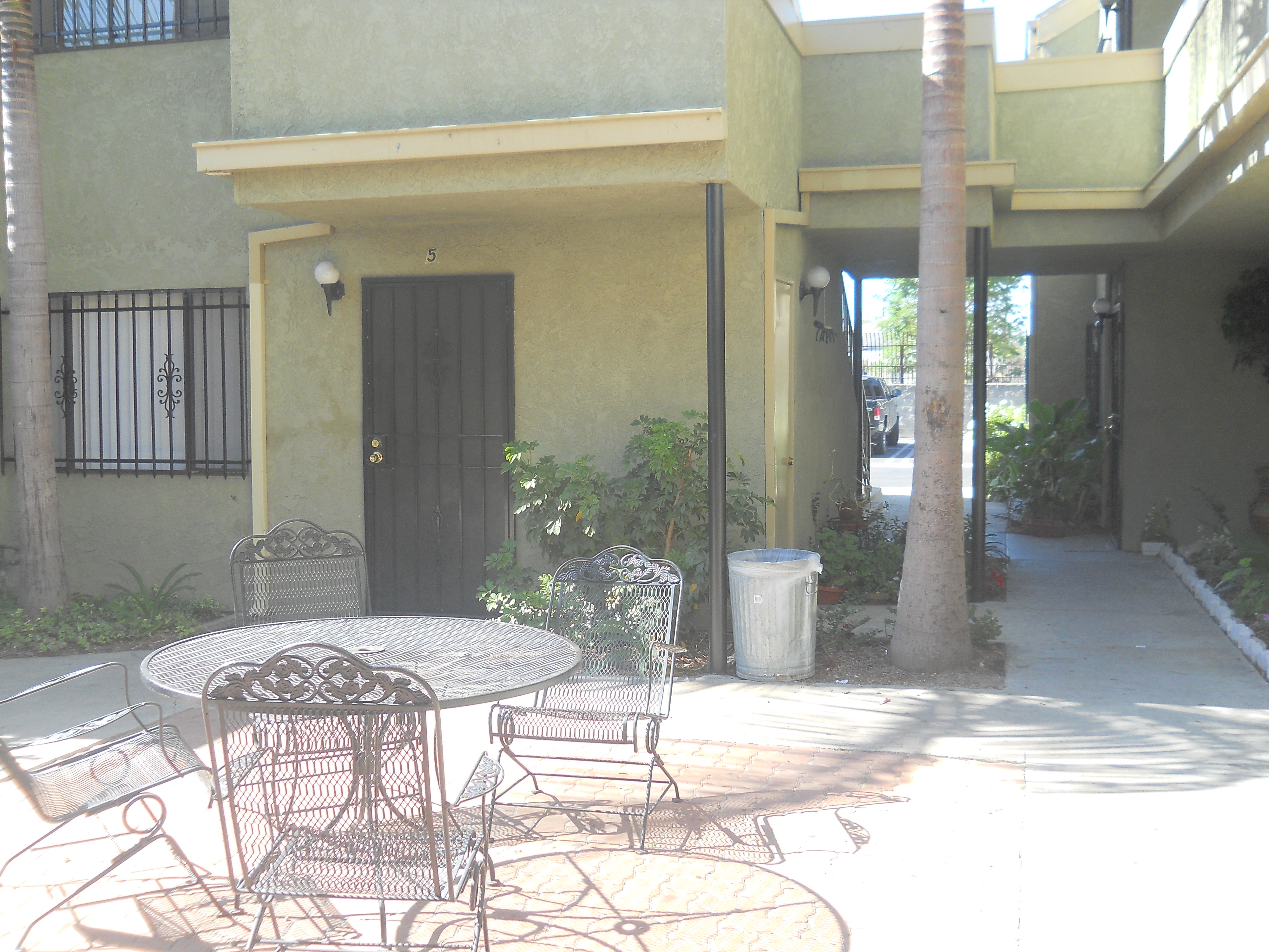 Nyumba Apartments, outside patio with a wrought iron patio table with four chairs, visible is a unit with a wrought iron door and parking area.