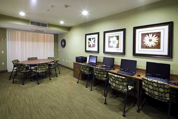 Interior image of Andalucia Senior Apartments commuity computer room showing 4 computers and an oval conference table with chairs