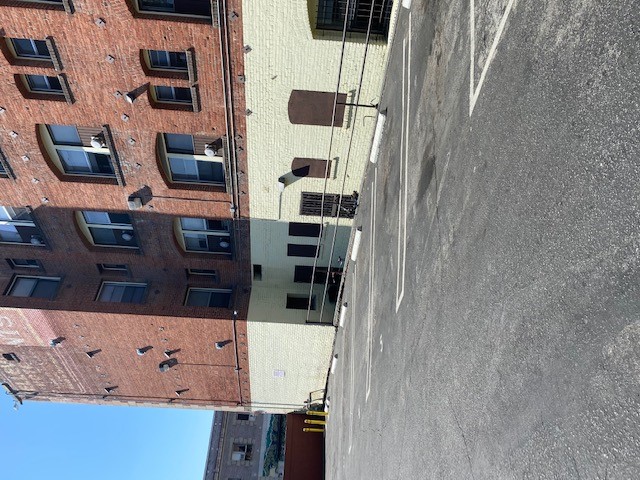 View of an outdoor parking lot a old fashioned four story brick building. Ground floor is painted white, and above floors are red. Side of the parking has a railing seperating the parking and the building.