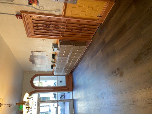 Lobby area with brown mailboxes. On top sits two small plants and a brochure stand. Entrance is ground floor, floor is wooden, there's a chandelier light on the ceiling, and there is elvator buttons visible.