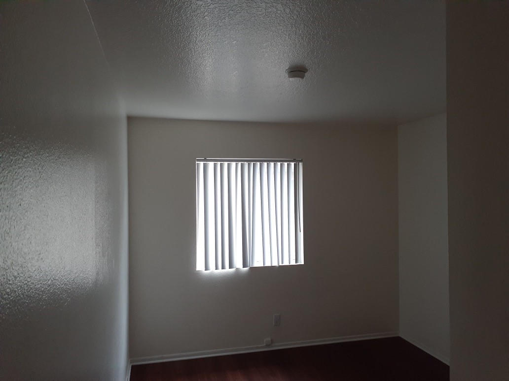 View of a unit, white walls, brown laminate floors, window with white vertical blinds.