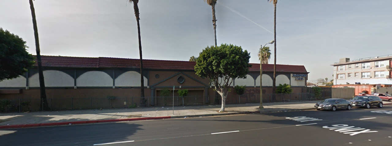 Street view of property. Multi colored building with palm trees lining the perimeter.