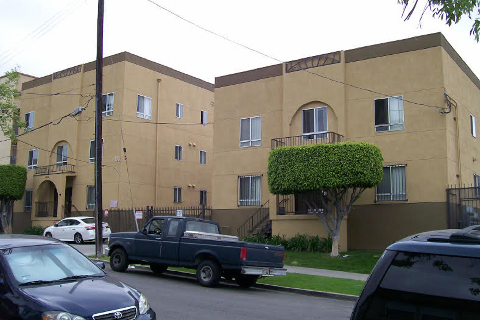 Right side view of two-building next to each other with a gated parking door in the middle, left side building is a three story and right side is a two story, multiple windows, bottom windows are gated, both building have a balcony in the middle, parked c