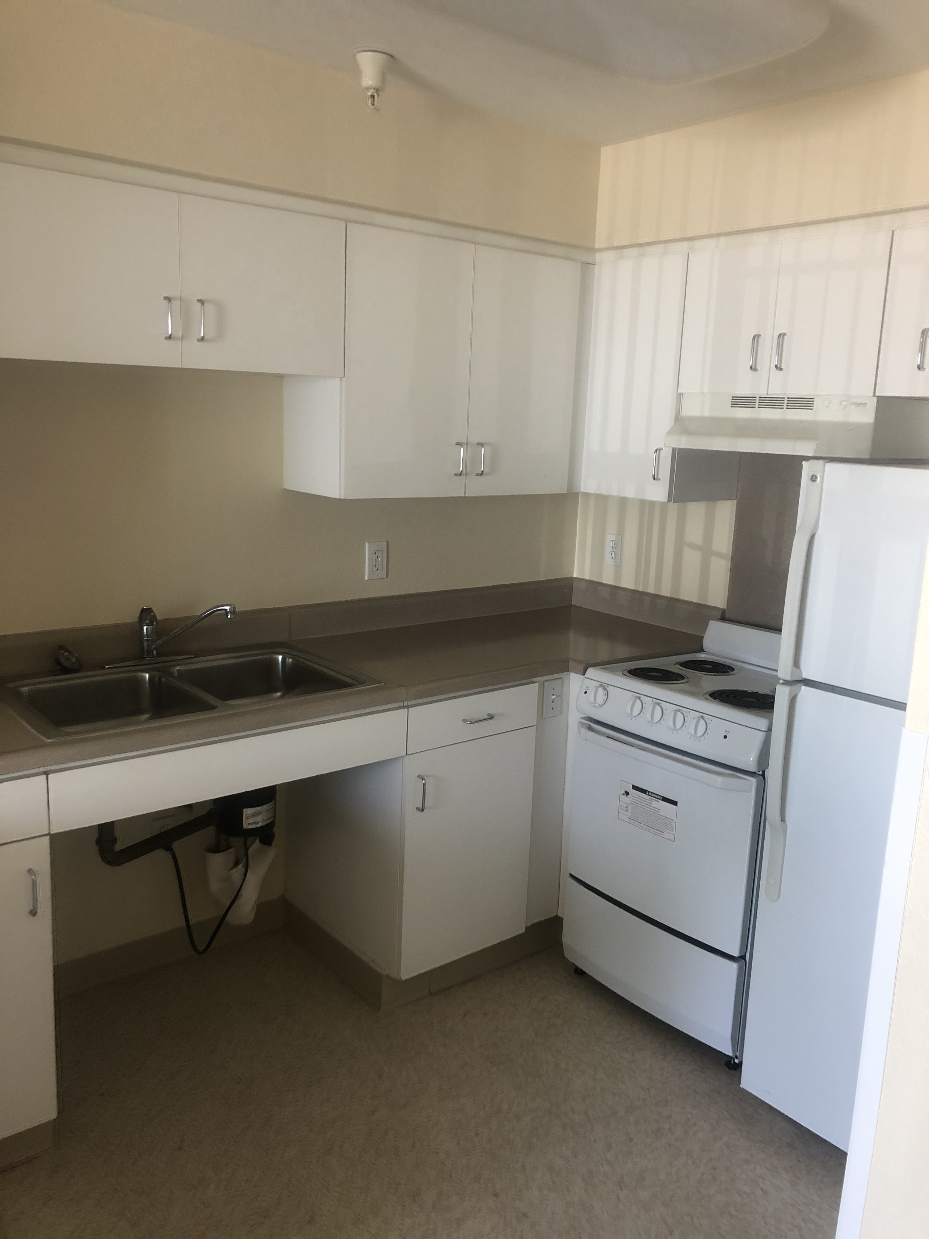 View of kitchen. Upper and lower cabinets, range stove, and fridge. Sink has open space underneath for wheelchair access.