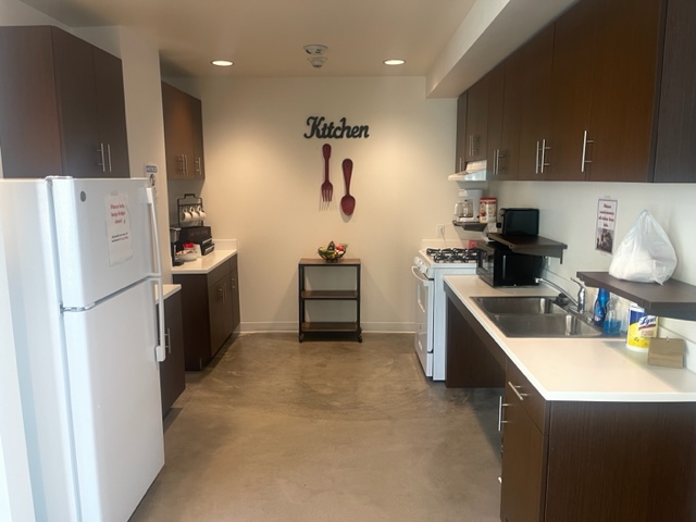 RDC- Full Size Kitchen. Refrigerator located on the right. Kitchen sink and counter top located on the right. Brown shelving above sink.