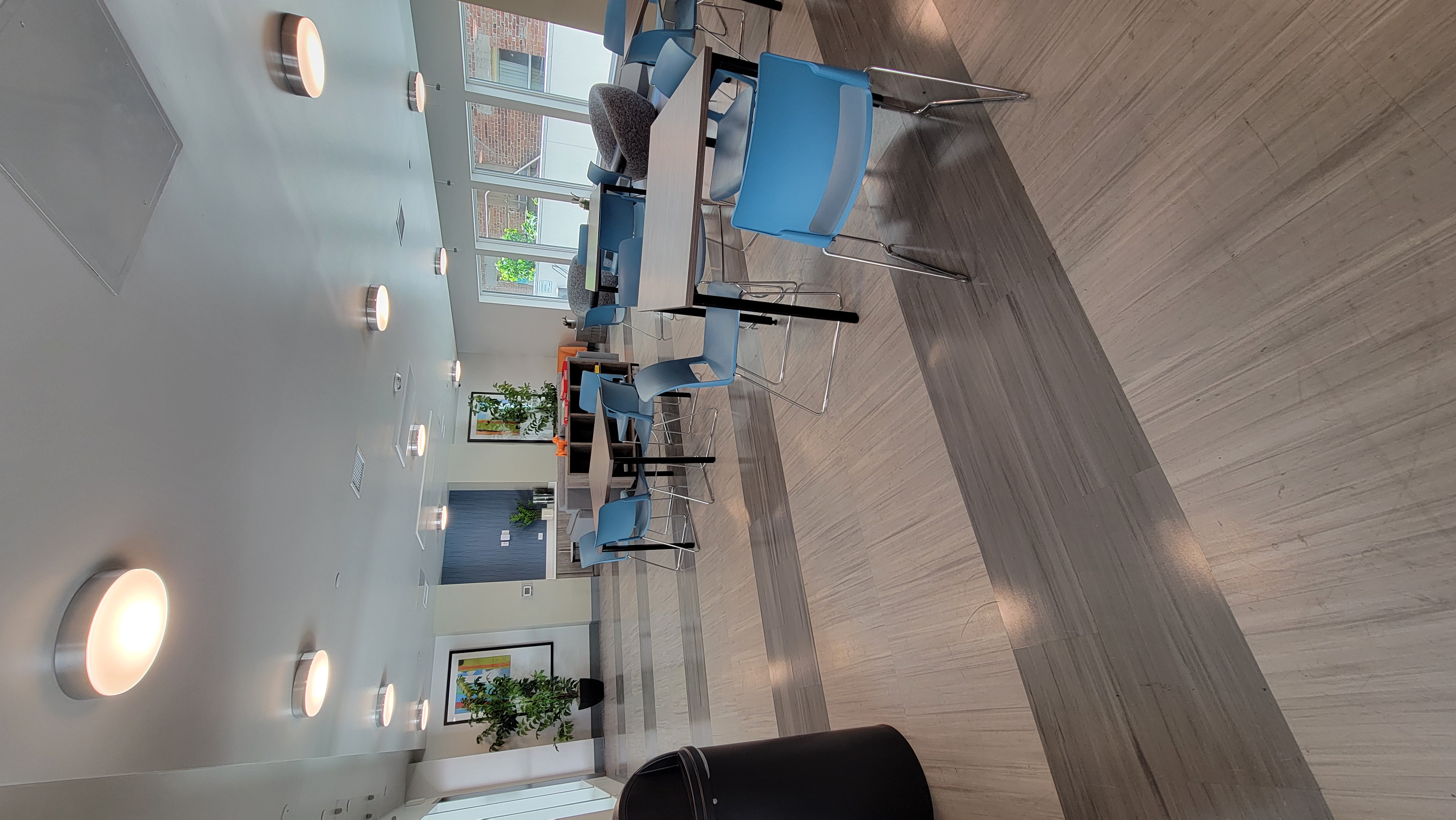 Community room with table and chairs for sitting in the center of the room. Windows on both sides allow light to enter the room.