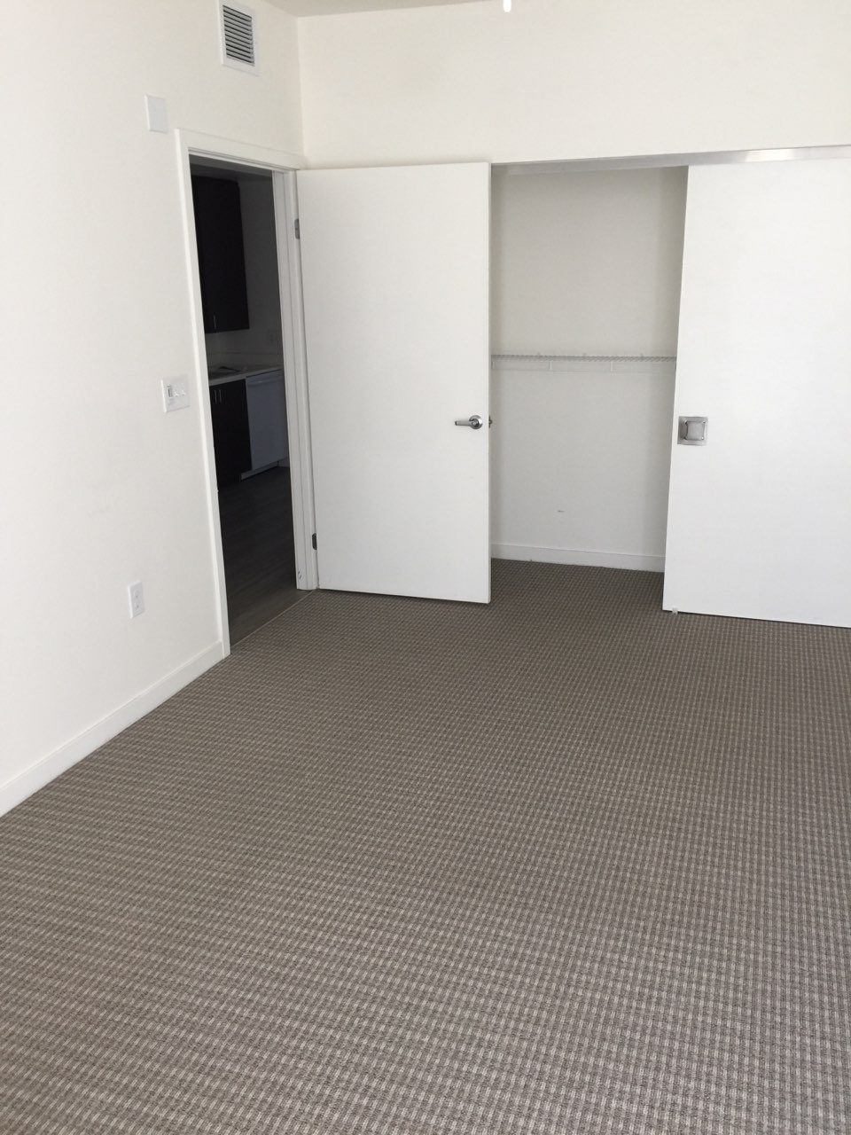 Inside view of a bedroom of a unit. Room has capet flooringand a closet with a sliding door. Walls are white.