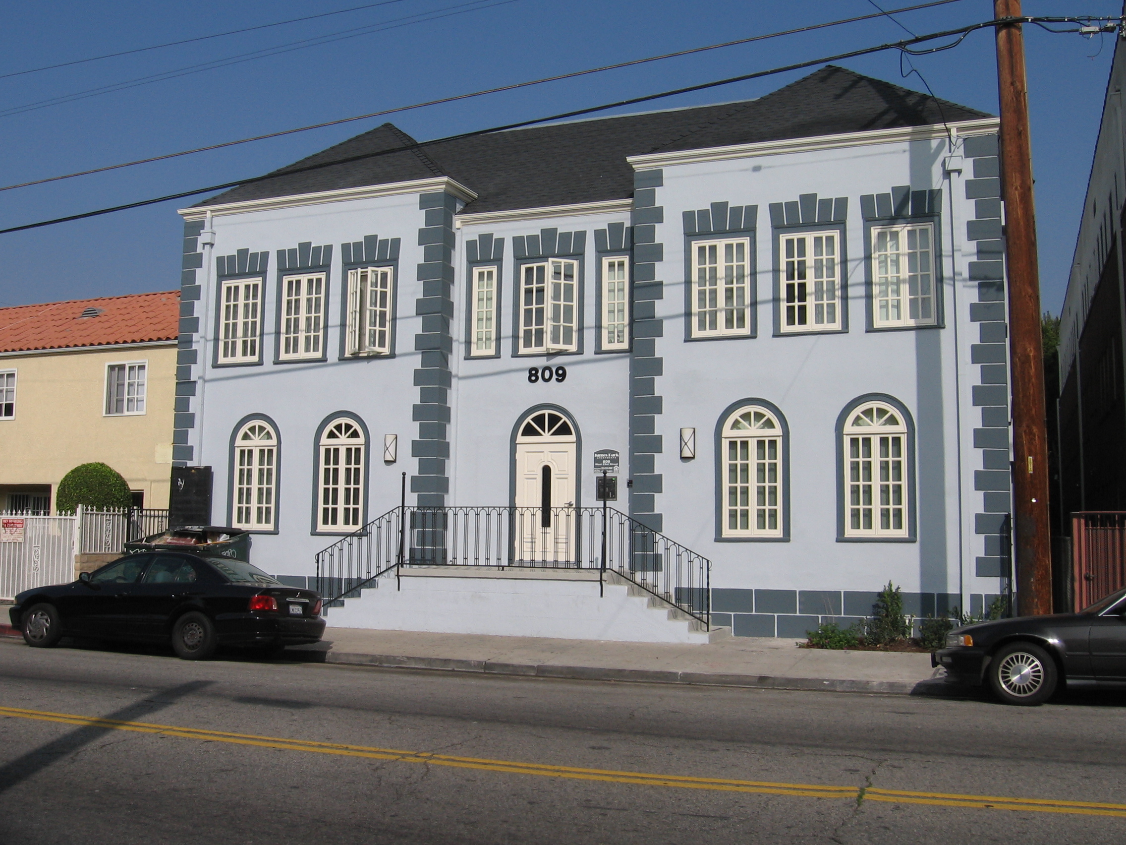 Street views of blue two story apartment building with stairs leading to the front door entrance