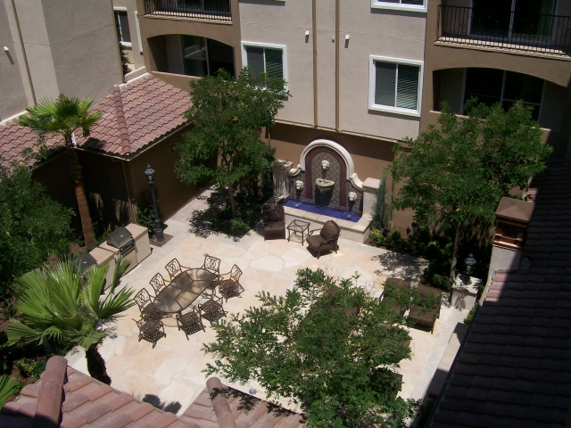 Image of apartmrnt building courtyard with patio table, chairs, water fountain and bbq grill