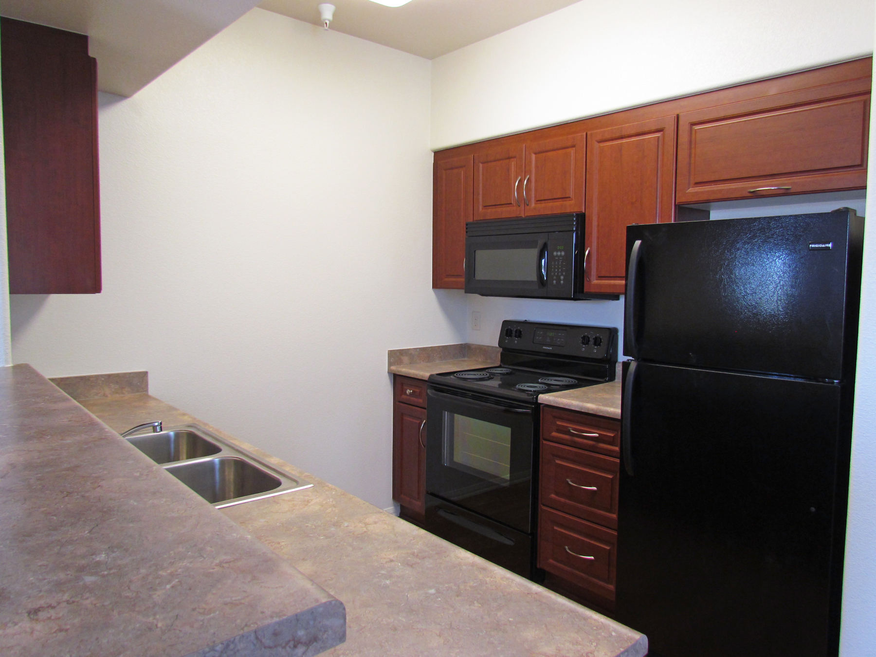 Interior view of a kitchen of a unit at Osborne Street Apartments. Refrigerator, microwave, stove, and on the opposite side is the sink and counters