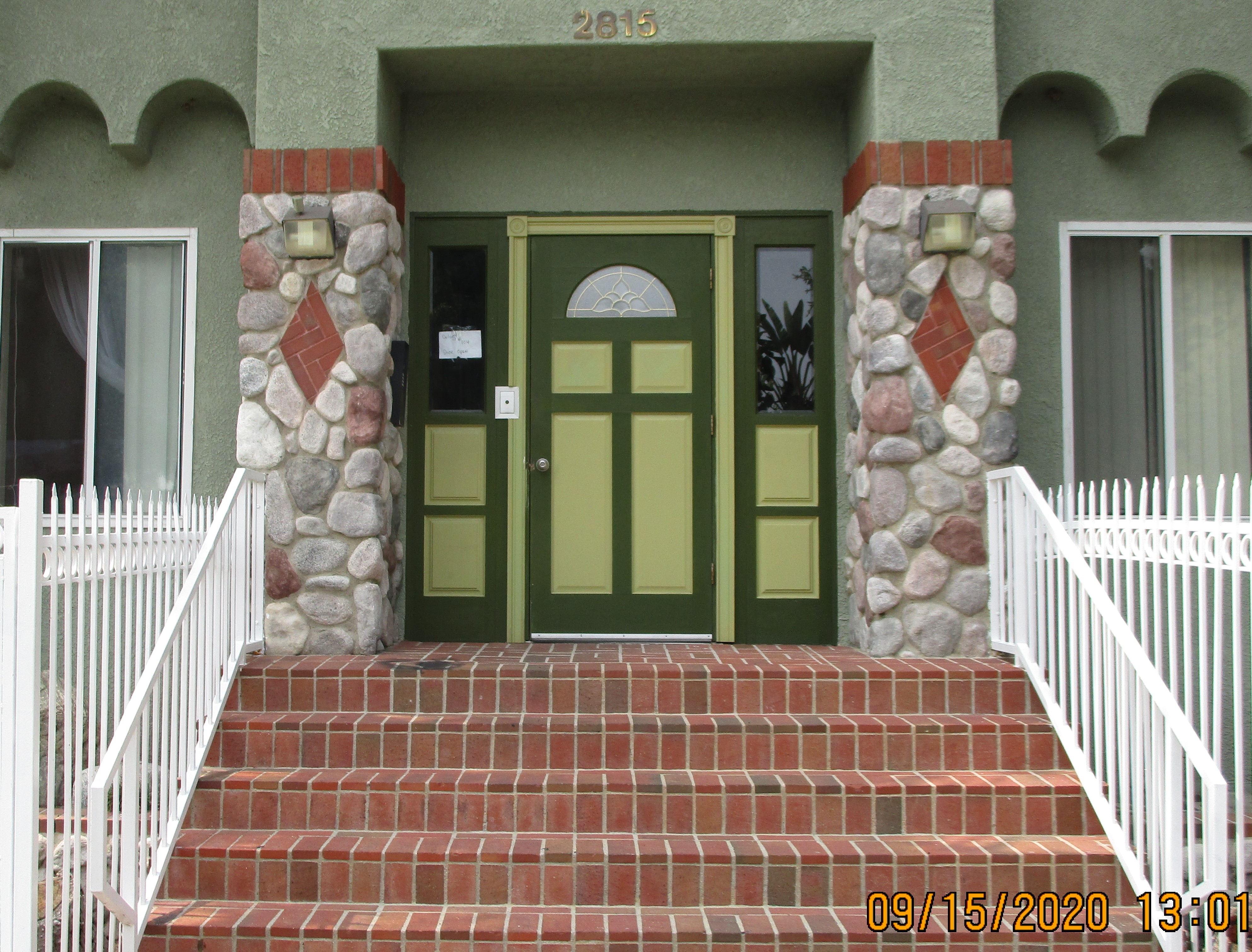 Front view of the green building entrance with brick stairs and white wrought iron fencing.