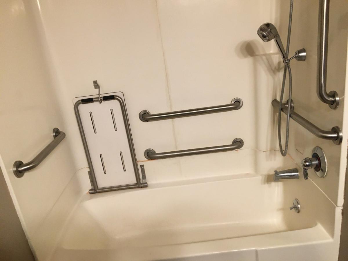 View of shower with multiple handle bars, lowered shower head, and in-shower seat.