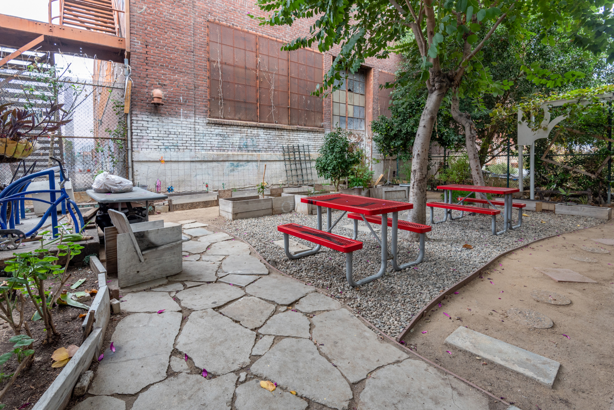 Exterior view of Las Americas, courtyard with 2 red picnic tables and a tree next to each tree