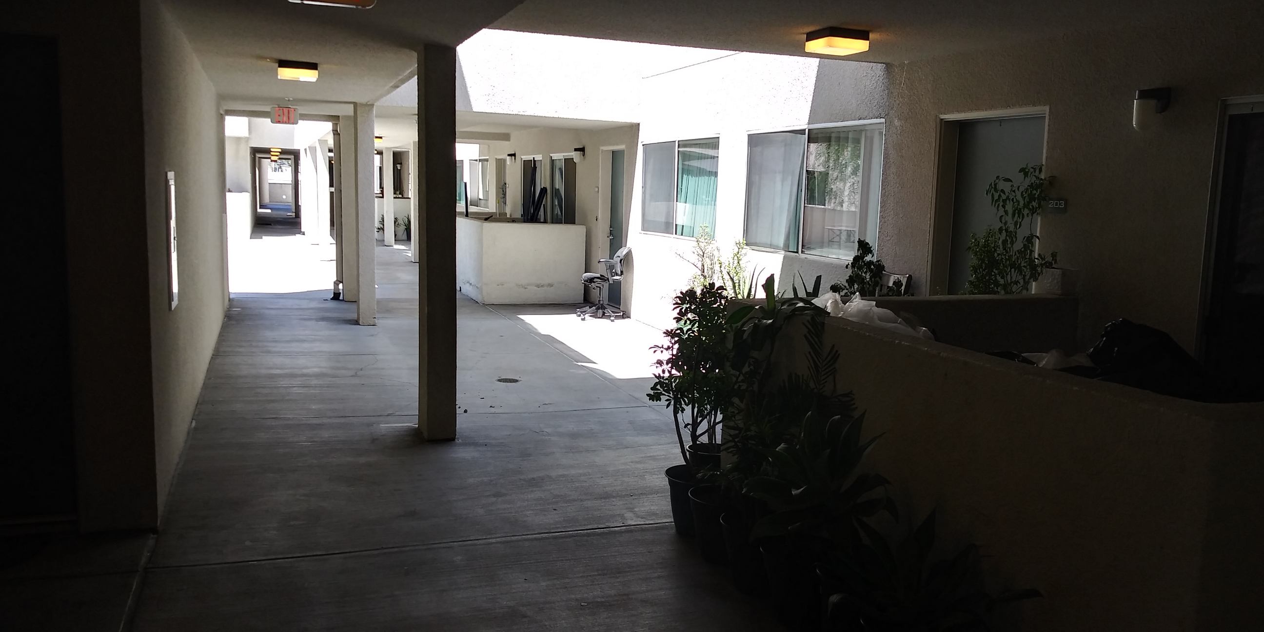 View of an outdoor passageway to units that is semi covered. Units have lounging spaces in front of them that are semi enclosed.