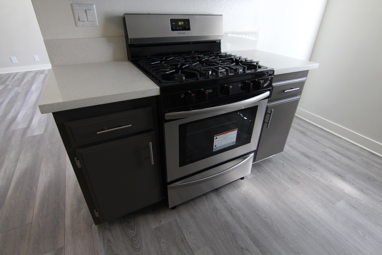 Picture of an oven stove with cabinets on the side. Floor is wooden.