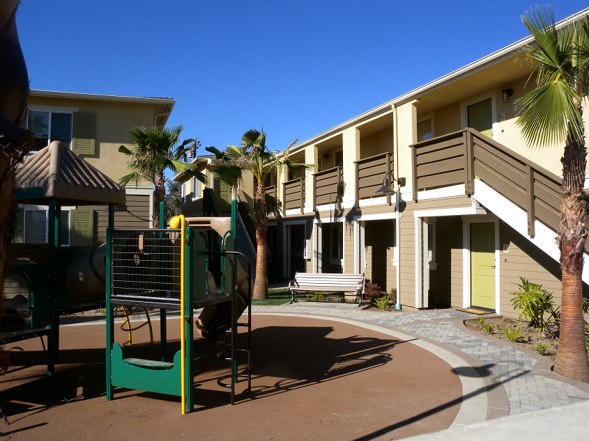 View of kids jungle gym play area on the properties premise. Park bench seating area and well maintained palm trees and plants along the inner part of double story building. Stariwell access to secod floor