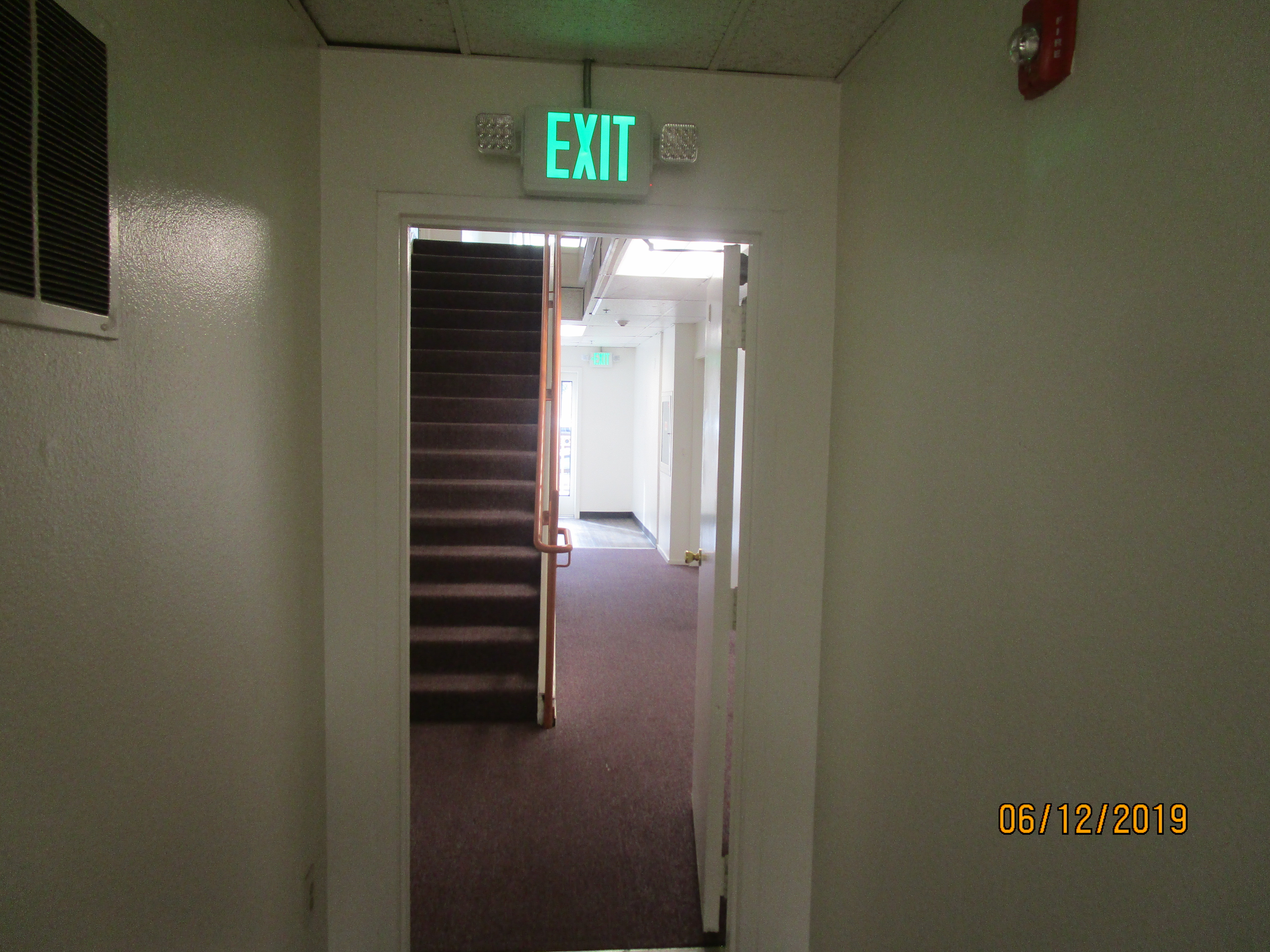 View of a hallway, stairs on the left side, doors and a exit on the right side.