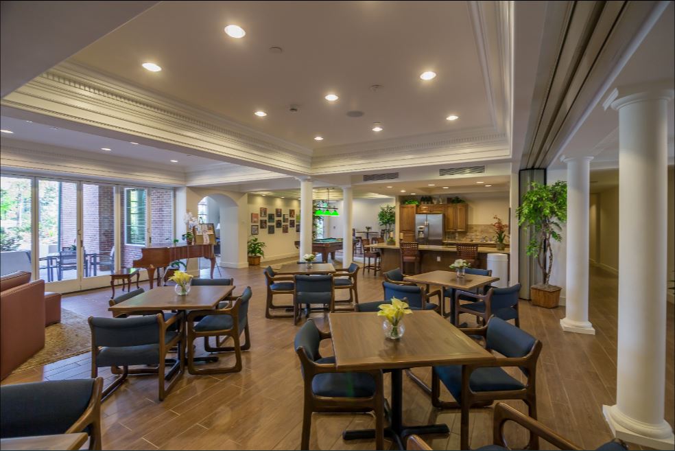 Large community room that has multiple table sets, a piano, pool table and a kitchen area. There is a door that leads to an outside lounging area as well
