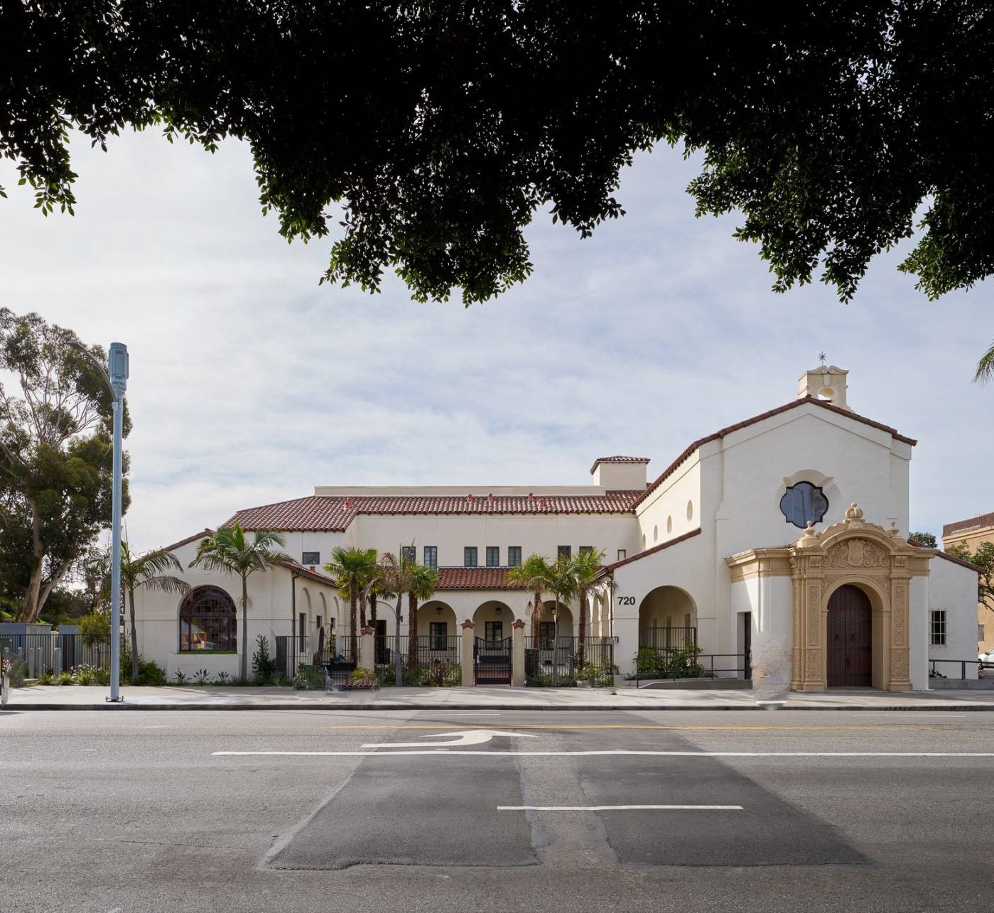 Exterior view of Washington View Apartments. It is a large white building with red-brown tile roof. Palm trees in a fenced courtyard are visible.