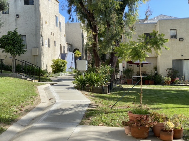 Exterior view of Imogene Coop. Housing showing a pathway in between potted plants and trees