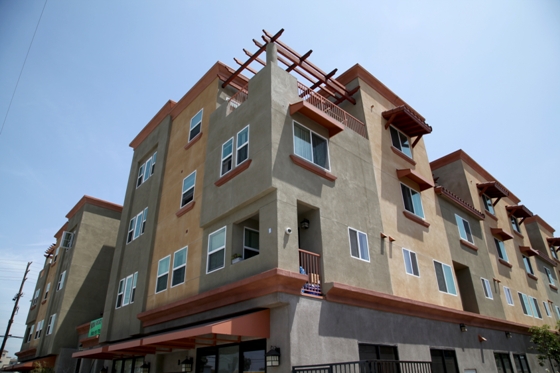 Street view of a three story building in brown and orange color. Top floor apartment have a open terrace and balcony