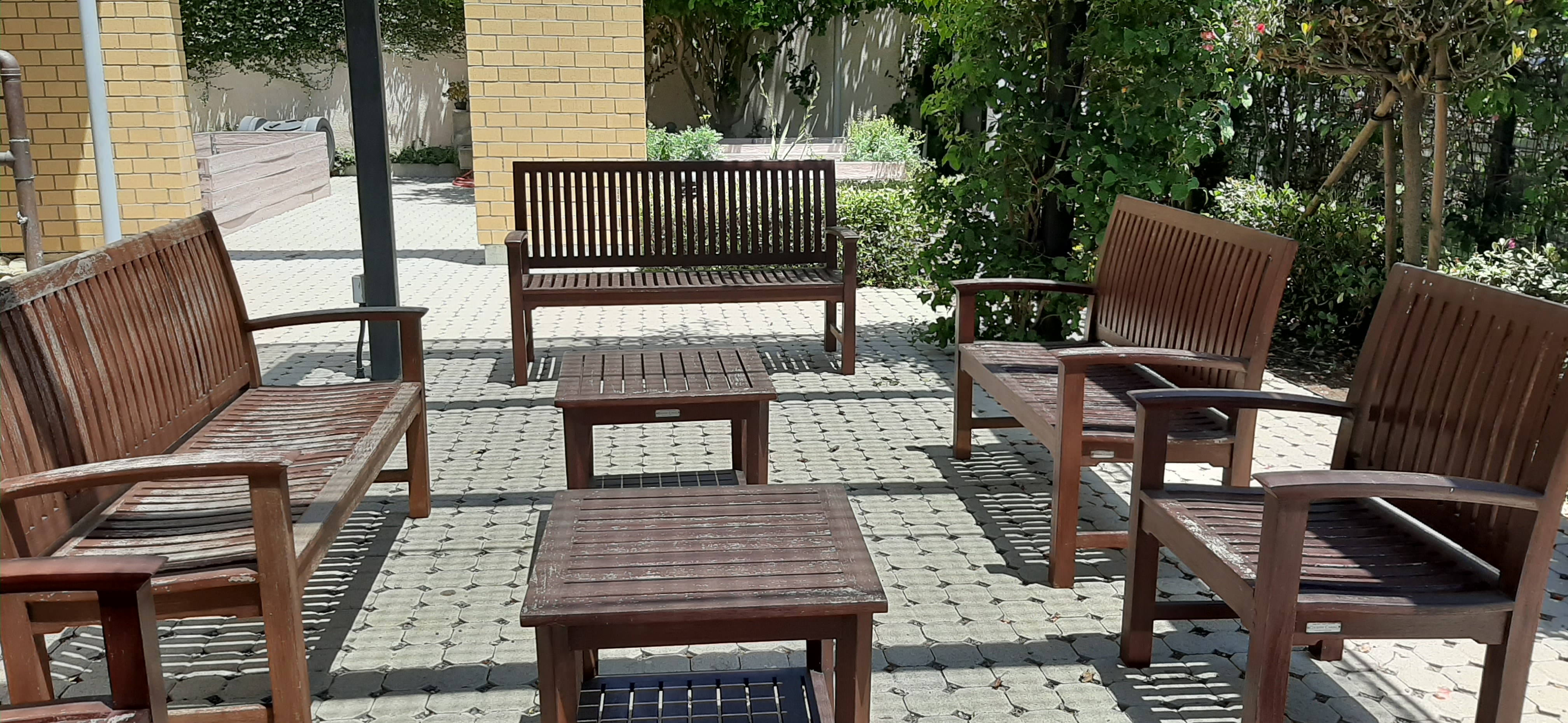 Willis avenue garden seating area. several picnic benches and small coffee tables. Flowers and tress around seating area.