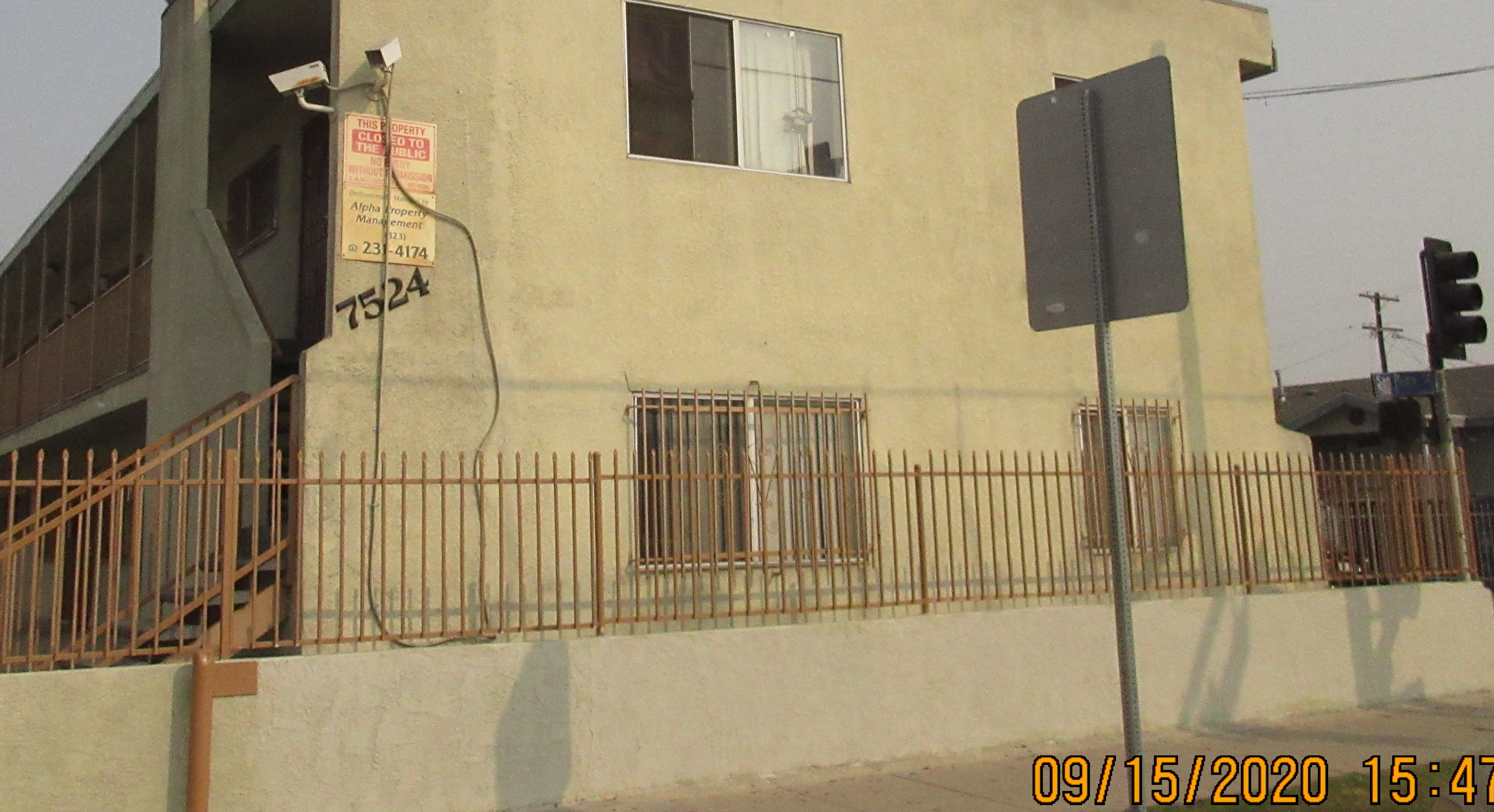 Right side view of an gated building, building number, camera, private property and management signs on the wall.