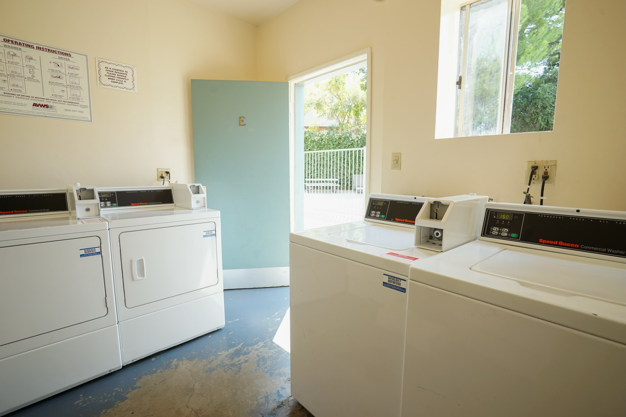 Laundry room with four machines visible. There is an operating instruction sign posted on the wall, and a sliding window.