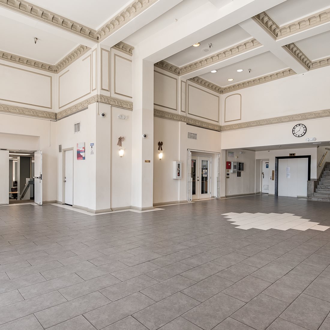 Spacious lobby area with an elevator and a staircase. This area has high ceilings, and security cameras.