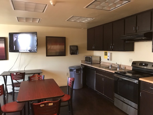 Interior view of the community kitchen at Lyndon Hotel. A stove, sink, Microwave, cabinetts, television, tables and chairs