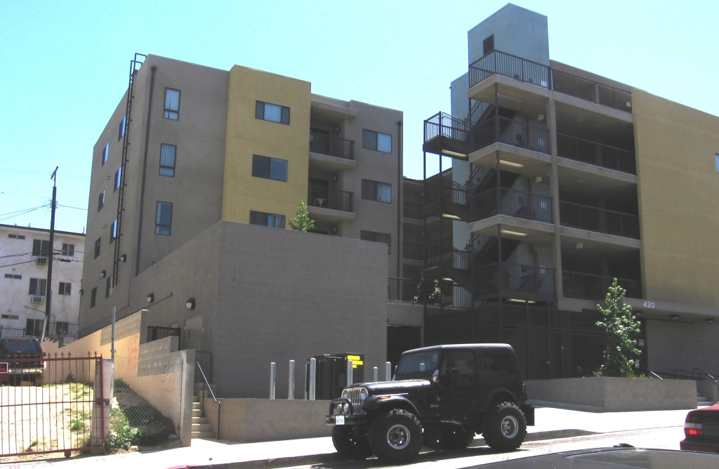 Four story brown and yellow apartment complex with gated parking on premises. Layout of complex contains outdoor stair ways between floors and balconies on some units.