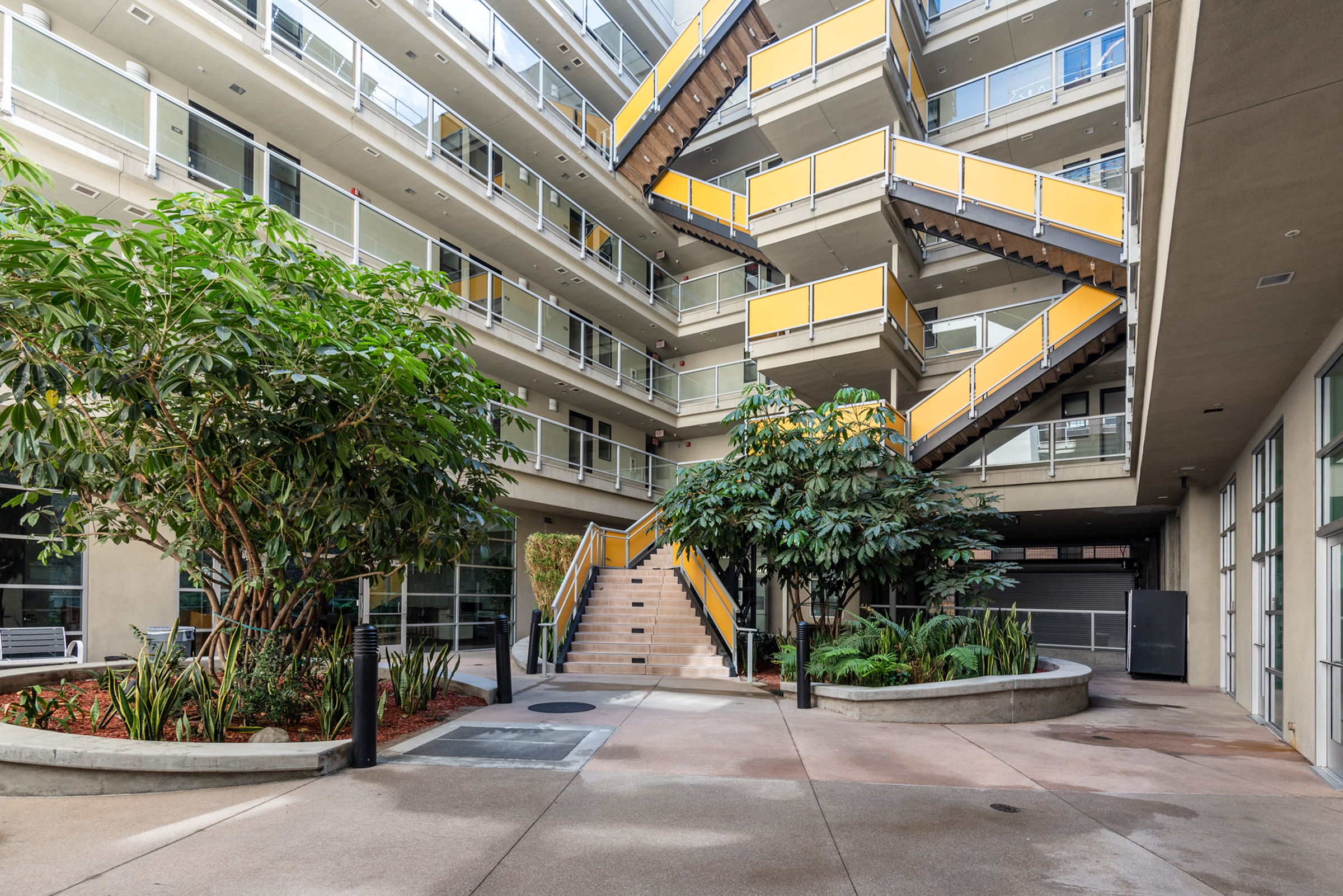 A front view of a zig zag type of stairs, multiple floors building, plants and bushes.