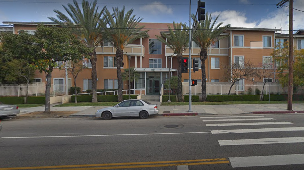 Street view of the Adams Congress Apartments,3 story tan building with a signal light and crosswalk in front